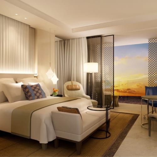 Luxurious hotel room with a large bed, seating area, and balcony overlooking a sunset view.