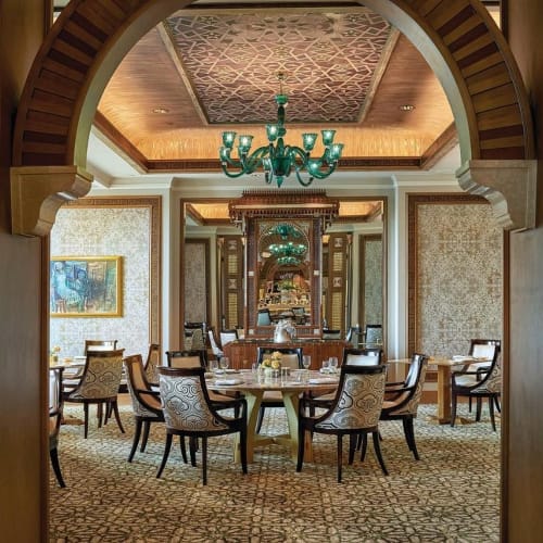 Elegant dining room seen through an ornate wooden archway with a central chandelier and a round table set for guests.