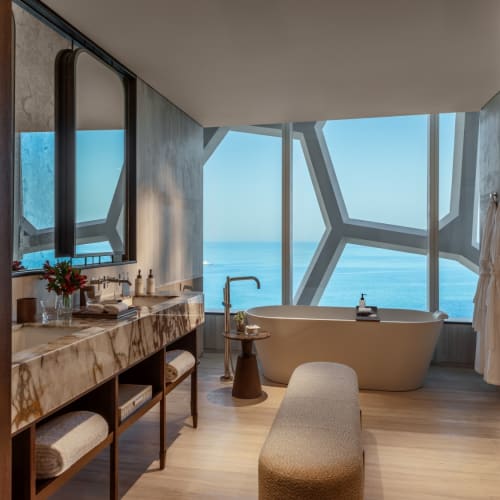 Luxuriöses Badezimmer mit freistehender Badewanne und großen Fenstern mit Meerblick im Rosewood Doha.