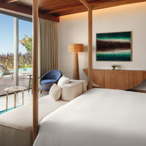 Ein luxuriöses Hotelzimmer mit großen Schiebetüren, die zu einer Terrasse und einem Poolbereich mit Palmen führen, modern eingerichtet mit einem bequemen Bett.