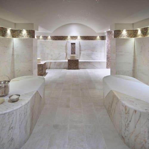 Ein luxuriöser Spa-Raum mit weißen Marmorbänken und einem zentralen Brunnen, beleuchtet mit sanftem Licht.