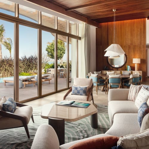 Exklusive Hotellobby mit großen Glasfenstern, die eine Strandansicht zeigen, moderne Möbel und eine Holzkonstruktion an der Decke.