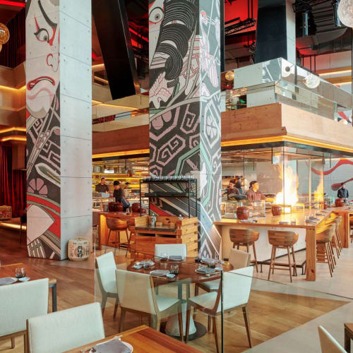 Moderner Restaurantinnenraum mit hölzernen Tischen und weißen Stühlen, dekoriert mit auffälligen gemusterten Säulen und hängenden kugelförmigen Lichtern.