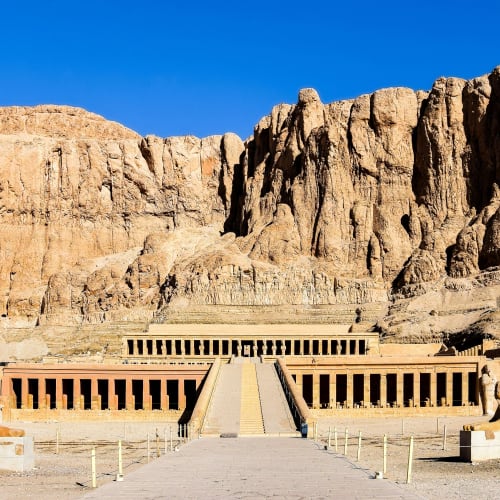 Der Hatschepsut-Tempel mit Bergkulisse in Luxor, Ägypten, mit einer großen Treppe und Sphinx-Statuen am Eingang.