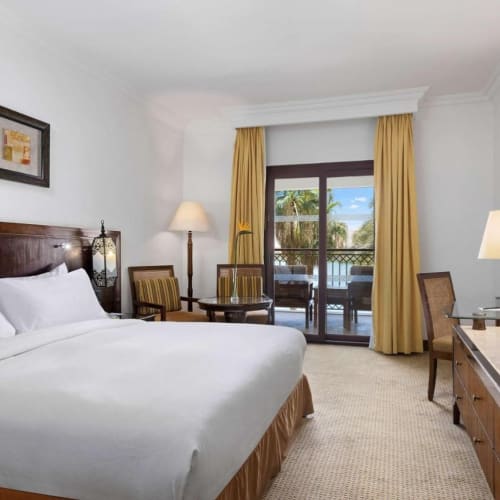 Spacious bedroom with a large bed, a balcony with outdoor seating, and modern furniture in a Hilton resort.
