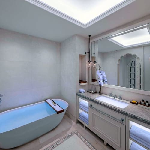 Ein luxuriöses Badezimmer mit einer frei stehenden Badewanne und einem großen Spiegel über einer Marmorkonterpane mit Handtüchern und Pflegeprodukten.