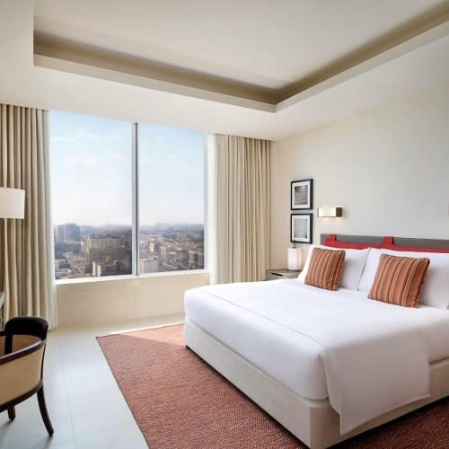 Ein modernes Hotelzimmer mit großem Bett, Stadtblick durch das Fenster und schlichter Dekoration.