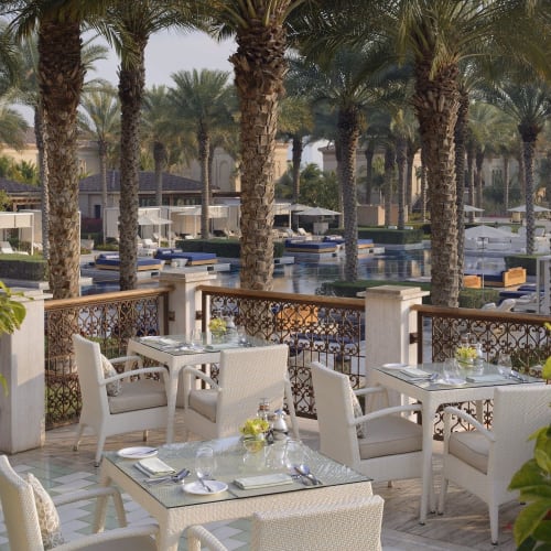 Elegant outdoor dining area overlooking a pool and palm trees at a resort.