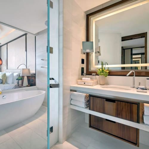 Ein luxuriöses Badezimmer mit großem Spiegel, moderner Spüle und Blick in ein stilvolles Schlafzimmer mit großer Badewanne.