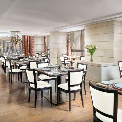 Eleganter Speisesaal in einem Hotel mit ordentlich gedeckten Tischen, großen Fenstern und dekorativen Vorhängen.