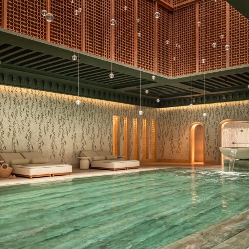 Indoor spa with a large turquoise pool, cushioned lounge chairs, and decorative wooden panels on the ceiling.