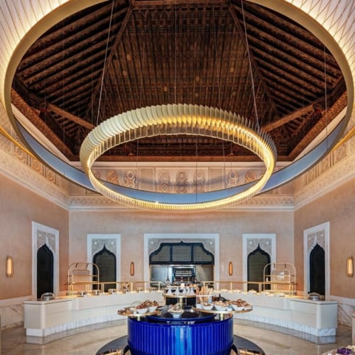 Luxuriöses Buffet-Setup in einem großartigen, kunstvoll dekorierten Saal mit einer großen runden Lampe an der Decke.