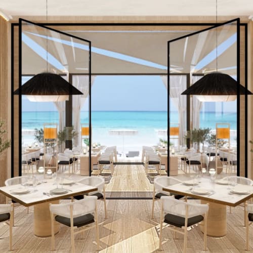 Elegantes Restaurantinnere mit großen Glasfenstern mit Blick auf einen Strand und den Ozean, mit runden und rechteckigen Tischen, Zimmerpflanzen und modernen Hängeleuchten.