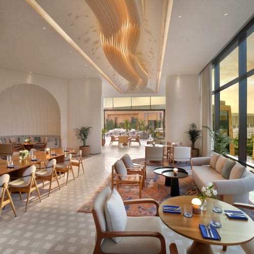 Moderner und eleganter Lounge-Bereich mit großen Fensterfronten, die bei Sonnenuntergang eine Stadtansicht bieten.