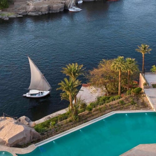 Blick auf einen Pool mit Blick auf den Nil, mit Palmen und einem Segelboot auf dem Fluss.