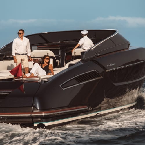 A luxurious black yacht with three people onboard, one standing and two sitting, cruising on the water under a clear blue sky.