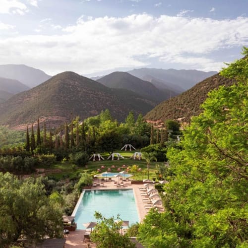 A scenic landscape with a swimming pool surrounded by lush greenery and mountains in the background.