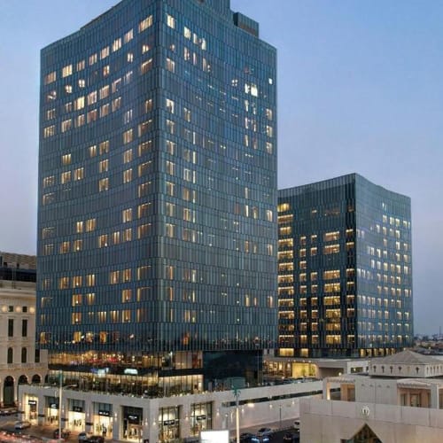 Modern glass skyscrapers in an urban setting during the evening, with lights on in many windows.