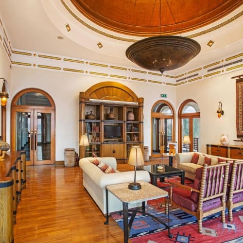 Elegantes Wohnzimmer mit weißen Sofas, Sesseln, Holzmöbeln und dekorativen Teppichen unter einer großen runden Decke.