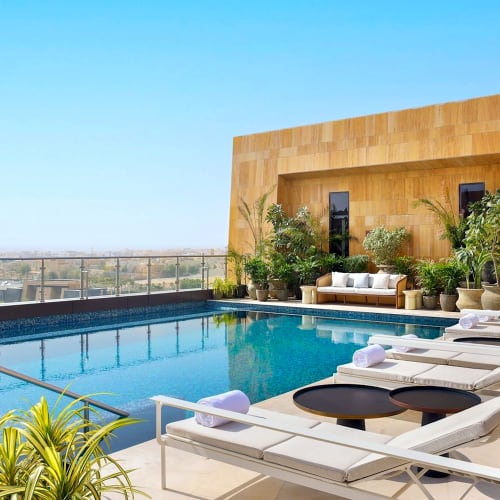 Dachterrassen-Außenschwimmbad im The St. Regis Riyadh mit Sonnenliegen, Sonnenschirmen und Blick auf die Stadt.