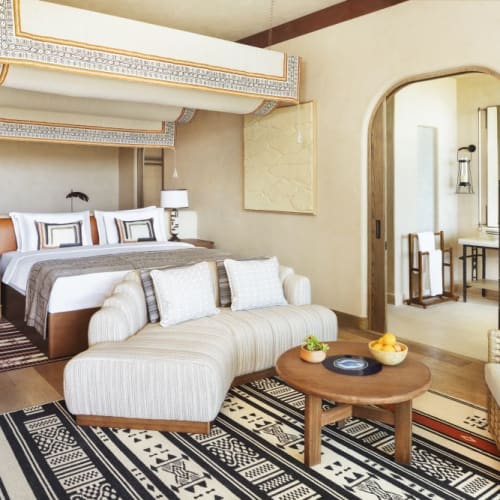 Luxurious hotel room with a double bed, sitting area, and decorative ceiling feature.