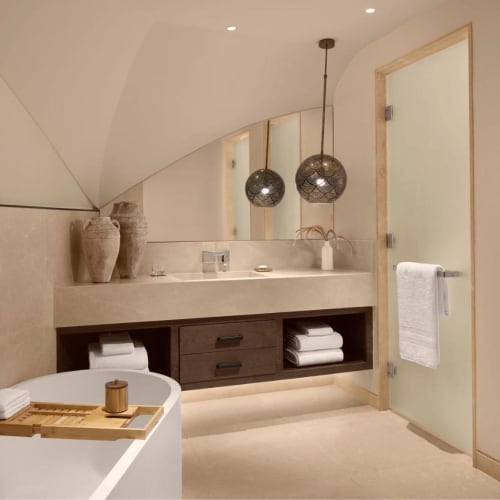 Ein modernes, minimalistisches Badezimmer mit freistehender Badewanne, großem Spiegel und zwei hängenden Pendelleuchten.