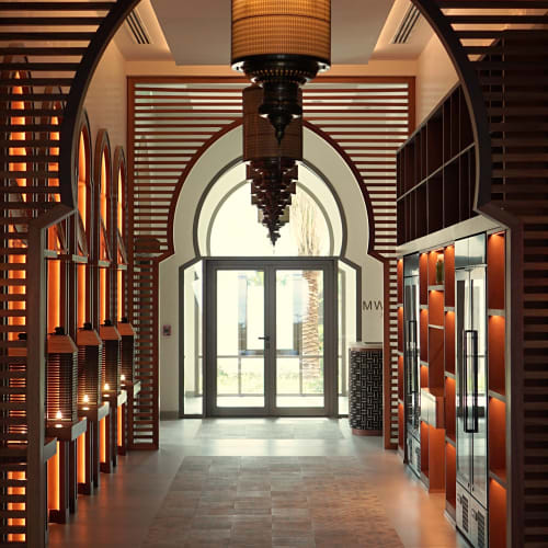 Ein schwach beleuchteter Flur mit gewölbten, holzverkleideten Wänden und Laternenlichtern, der zu einer hellen Glastür im Weinkeller von Naäma Beach Villas und Spa Aseelah führt.