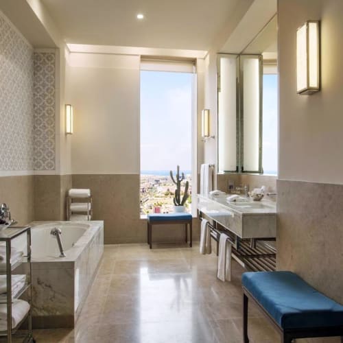 Spacious bathroom in a luxury hotel suite with a bathtub, large window, and elegant lighting.