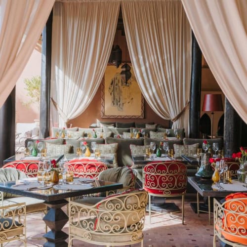 Elegantes Restaurant-Innenraum mit gewellten Vorhängen und bunt gemusterten Stühlen, die um gedeckte Tische sitzen.