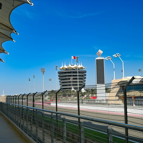 Blick auf die Bahrain-Formel-1-Rennstrecke mit Haupttribüne und modernen Gebäuden unter klarem blauen Himmel.