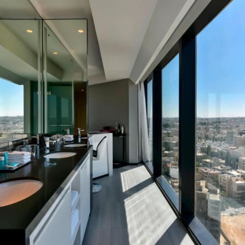 Modernes Badezimmer mit großen bodentiefen Fenstern, die die Stadtsilhouette von Amman überblicken.