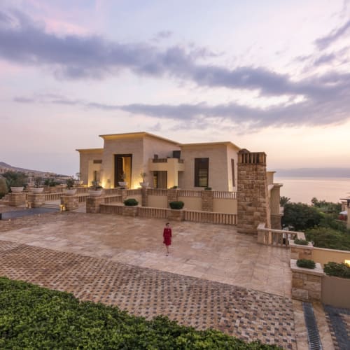 A luxurious hotel building overlooking the Dead Sea with modern architecture and a spacious terrace at sunset.