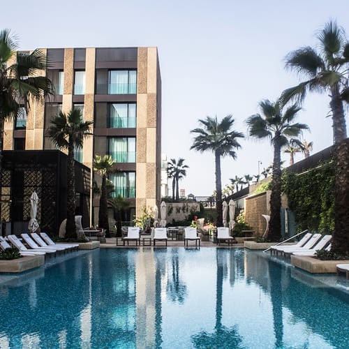 Ein luxuriöser Hotelpoolbereich mit Palmen und Liegestühlen vor einem modernen Gebäude.