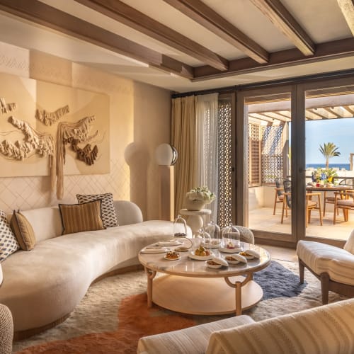 Luxuswohnzimmer mit modernem Dekor, beigem Sofa und Schiebetüren, die zu einem Balkon mit Meerblick führen.