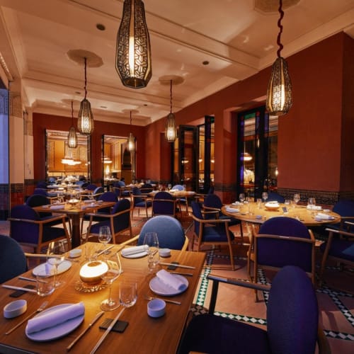 Elegantes Restaurantinnere mit warmem Licht, blauen Stühlen und ausgedeckten Holztischen zum Essen.