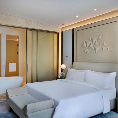 Luxuriöse Hotellounge mit einem großen Bett, moderner Dekoration und einem offenen Badezimmer mit freistehender Badewanne, sichtbar durch Glastrennwände.