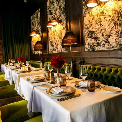 An elegant indoor restaurant setting with a long table decorated with flowers, glassware, and tableware, illuminated by warm lighting.