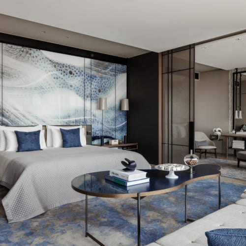 Ein modernes Hotelzimmer mit einem großen Bett, einem Sofa, einem Glastisch und dekorativer Wandkunst in Blau und Weiß.
