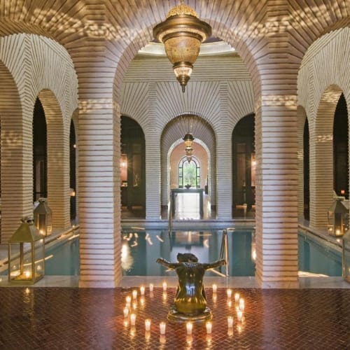 Luxurious indoor spa area with arches, a central statue, and warm lighting in a Moroccan-style setting.