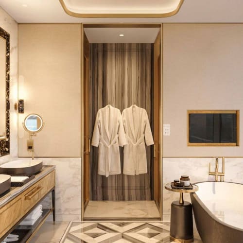 Luxuriöses Hotelbad mit Doppelwaschbecken, Badewanne und Flachbildfernseher, dekoriert mit Goldakzenten und Marmorböden.