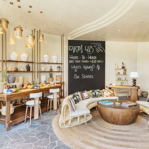 A cozy indoor lounge with a curved sofa, a round coffee table, a large blackboard, and a wooden dining table with chairs.