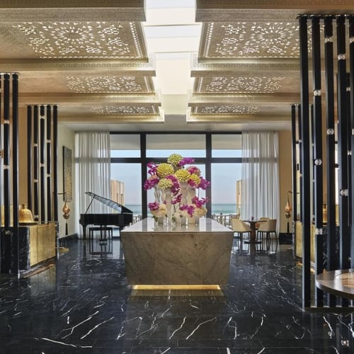 Luxurious hotel lobby with a grand piano, modern decor, and a large window view of the sea.