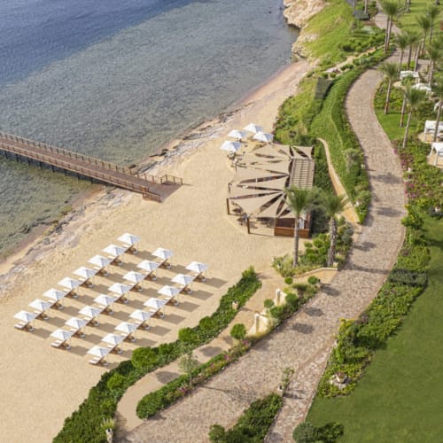 Luftaufnahme eines Four Seasons Resorts in Sharm El Sheikh mit Strand, Sonnenliegen, einem Holzsteg und üppigem Grün.