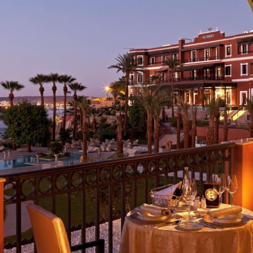 Ein romantisches Abendessen auf einem Balkon mit Blick auf ein Resort mit Palmen und einem Pool bei Sonnenuntergang.