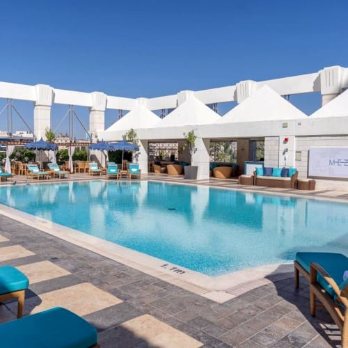 Ein luxuriöser Dachpoolbereich im Four Seasons Hotel Amman mit weißen Zelten und blauen Liegestühlen unter klarem blauen Himmel.