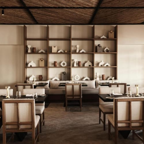 Modern restaurant interior with wooden shelving decorated with pottery and a long table set for dining.