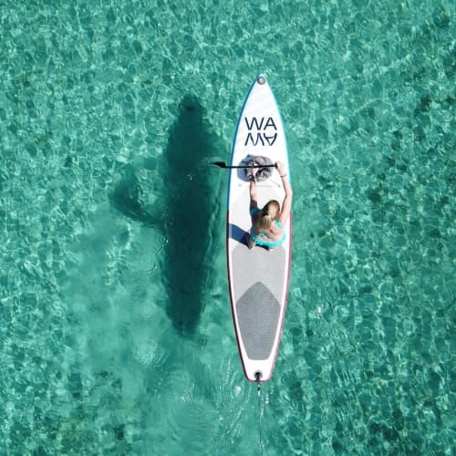 Eine Person auf einem Paddleboard in klarem, bläulich-grünem Wasser, sichtbar aus der Vogelperspektive.
