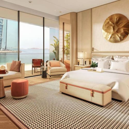 Luxurious hotel room with a large window view of a cityscape and a water body, featuring elegant furnishings and decor.