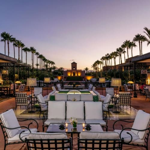 Elegant outdoor lounge area at sunset with palm trees, comfortable seating, and ambient lighting.