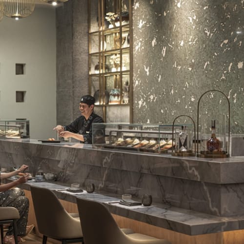 Two customers sitting at a marble bar counter in a luxurious restaurant at the Four Seasons Resort Sharm El Sheikh, with staff serving behind the bar.